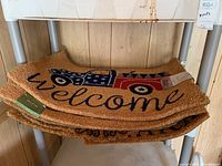 Stack of five coir welcome door mats with patriotic truck design, showing natural brown coir fibers and black welcome text.