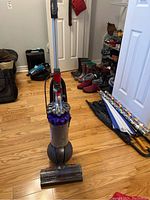 Full view of Dyson Smartball vacuum cleaner standing upright on hardwood floor with shoes and umbrellas in background.