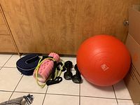 Photo showing all fitness items: orange exercise ball, black 10 lb weights, pink foam roller, green skipping rope, and blue neck pillow.