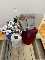 Full lot showing assorted linens stacked in a blue bin, two grey felt baskets, burgundy throw, floral patterned basket, and portable electric fan heater in front.