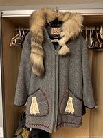 Full view of gray wool coat hanging in closet with fur trimmed collar and animal patches on pockets.