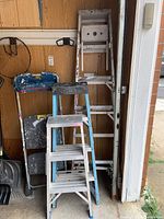Four ladders shown with two step ladders at front and two extension/step ladders behind. Aluminum construction and steel blue paint identified.