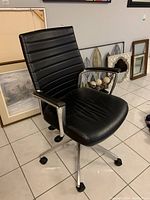 Front angle view of the black office chair showing padded backrest and seat, metal armrests with vinyl padding, and caster wheels.