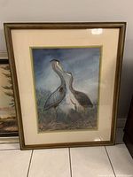 Framed painting showing whole artwork of herons in nest with mat and gold-tone frame.