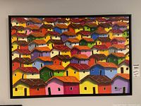 Full view of the framed colorful painting showing many small houses with red and brown roofs packed closely together.