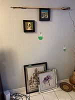 Three wooden arrows with feather fletching mounted horizontally on a wall above framed prints. Visible framed prints include a dog portrait and colorful geometric print.