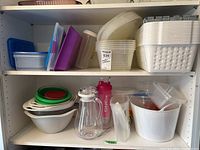 Two shelves with assorted plastic containers, bowls, plastic baskets and two water bottles arranged on shelves.