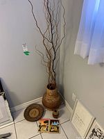 Large brown textured Mexican clay floor vase with dried branches inside, placed in a corner next to other pottery items and framed artworks.