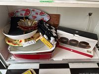 Photo showing assorted roasting pans, cutting board, grilling planks, serving platters and bowls including a watermelon-patterned bowl and a clear glass leaf-shaped dish.