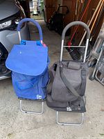 Two travel dollies shown side by side against garage setting, one blue, one black/gray with padded handles and metal frames