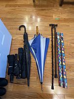Photo of four umbrellas, two walking canes, and two rolls of colorful balloon-pattern gift wrap on wooden floor.