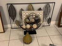 Lot including metal leaf wall art, decorative mirror with geometric frame, black wire basket with decorative spheres, and green ceramic vase.