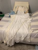 Vintage white wedding dress with lace detail laid out in box on a bed, showing full skirt and lace edging.