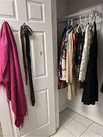 View of hanging clothes including vintage cocktail dress, sweaters, shawls on hangers inside closet.