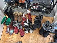 Photo showing all 8 pairs of boots arranged on floor and shoe rack, including black Hunter rain boots and various winter boots with fur lining