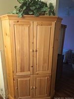 Closed front view of the large pine armoire showing four paneled doors with round wooden knobs.