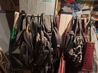 Wide shot of the Tommy Hilfiger clothes rack loaded with assorted bags including backpacks, handbags, and shoulder bags hung along the rack bar.
