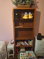Front view of a 5-level wooden bookshelf with various items including books and decorative pieces on and around it.