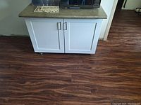 Front view of white cabinet with two doors and green countertop, positioned on wood flooring.