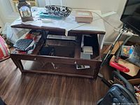 Full view of the wooden coffee table with the top lifted, showing the storage interior and lower shelf filled with household items