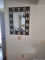 Rectangular mirror hanging on wall reflecting interior room including window and curtain.