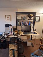 Wide view of the office setup showing the desk, computer, keyboard, mouse, bookshelf, and chairs.