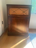 Front view of the antique Bendix cabinet showing the woven fabric panel and wooden door below.