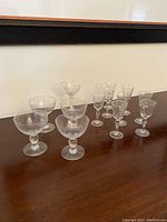 Fifteen small clear crystal stemware glasses arranged on a dark wood surface.
