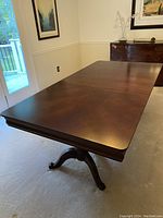 Full view of mahogany dining table with leaf extended showing rectangular top and pedestal legs