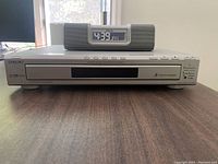 Front view of silver Sony five-disc DVD player with digital alarm clock placed on top, showing clock display and controls