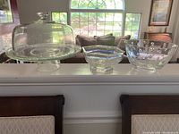 Photo showing all three glass items on ledge: cake dish with dome, small hexagonal bowl, larger bubble-pattern bowl.