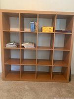 Front view showing 16 square compartments with some containing books and boxes, wooden finish.