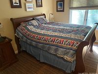 Side view of Queen size heavy oak sleigh bed with mattress on, covered in a patterned comforter and pillows.