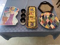 Photo showing six assorted serving trays on a table, including one shaped like a woman in sunglasses and basket, black plastic hexagonal tray, and ceramic trays with patterns.
