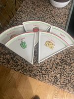 Five triangular ceramic plates shaped like pizza slices with painted toppings labeled: Mushroom, Tomato, Pepper, Onion, Cheese. Arranged in a semi-circle on a granite countertop.