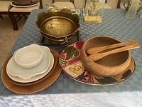 Wide view of lot showing all items on a blue checkered tablecloth including brass platter, wooden salad bowl with servers, nested white plates and bowls, and decorative ceramic platter.