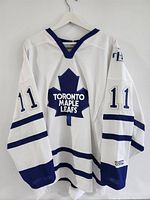Full front view of white Toronto Maple Leafs jersey showing blue maple leaf logo and number 11 on sleeves.