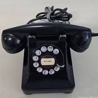 Front view of black rotary dial telephone showing dial numbers, alphabet letters, and paper with phone number inside central window.