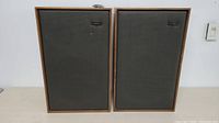 Pair of vintage Goodmans speakers side by side against a white wall, showing full front view with wood frames and black fabric covers.