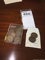 Clear top view of plastic container holding multiple circulated Newfoundland pennies, two PEI pennies from 1871 placed on handwritten note beside container.