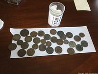 Coins spread out on white paper with coins in container next to them, showing overall lot contents and quantity.