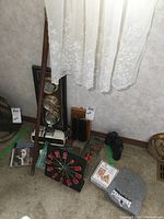 Overview of items including wall barometer, binoculars, shoe brushes, clocks, and various small items arranged on floor under window with lace curtain