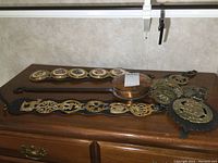 Photo showing multiple brass wall hangers with various decorative motifs and the small copper bed warmer on a wooden surface.