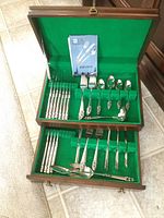 View of complete cutlery set in wooden chest with green felt lining showing knives, forks, spoons, and serving pieces along with instruction booklet.