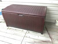 Full view of the brown Suncast resin deck box on a wooden deck, showing its rectangular shape with the hinged lid closed.