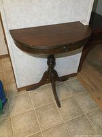 Front view of vintage demi lune half round table showing drawer and pedestal base with three legs.