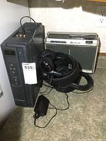Autovision vertical VCR with remote and cords, vintage cassette radio player, and headphones on floor.