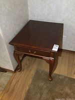 Wood end table showing top, drawer front with brass handle, and one side with cabriole legs.