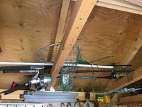 Photo showing four fishing poles stacked above a workbench, three have spinning reels attached and one pole has no reel. Included is a small green fishing net with metal frame.