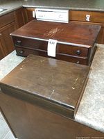 Two vintage wooden chests on countertop, larger 2-drawer chest on top and smaller chest in front, showing worn wood surfaces with scratches